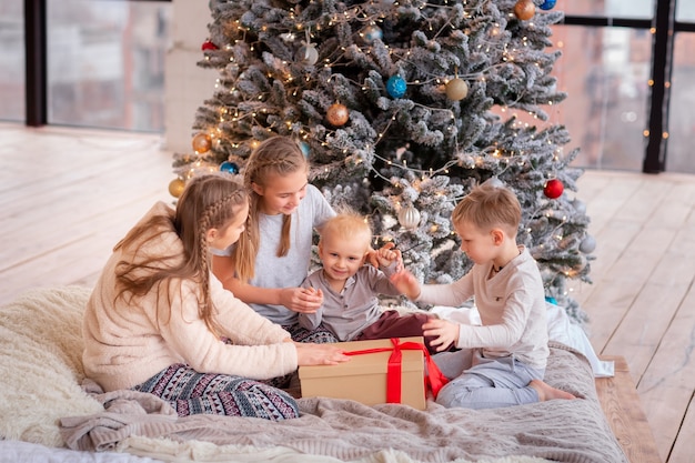 Des enfants heureux s'amusent et ouvrent des cadeaux près de l'arbre de Noël.