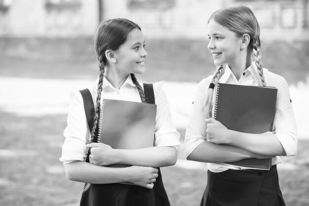 Des enfants heureux en uniforme scolaire tiennent des livres d'étude à l'extérieur, à la bibliothèque.