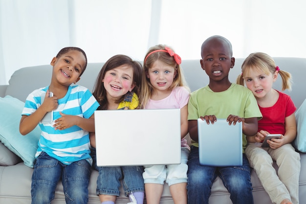 Enfants heureux en utilisant la technologie tout en étant assis sur le canapé