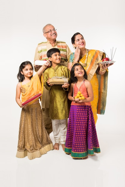 Enfants indiens avec des grands-parents en tenue traditionnelle tenant des cadeaux, des bonbons et du puja ou du pooja thali ou prenant un selfie, isolé sur fond blanc