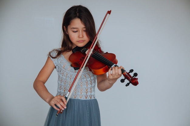 Enfants et instruments de musique Petite fille brune dans une belle robe jouant du violon à l'intérieur
