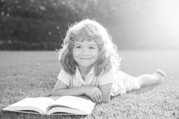 Enfants intelligents mignon garçon lisant un livre allongé sur l'herbe enfant lisant un livre dans le parc d'été