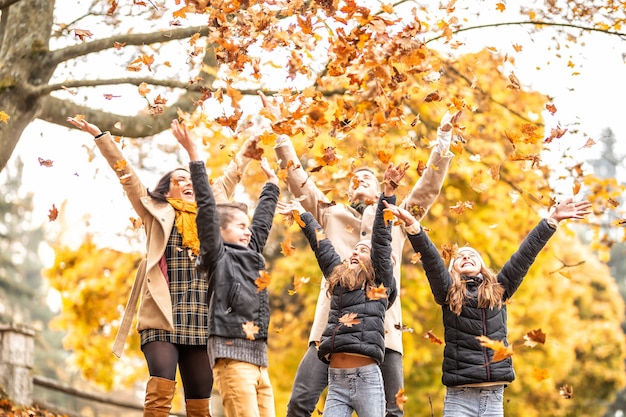 Des enfants jettent des feuilles colorées en l'air avec leurs parents à l'extérieur pendant l'automne.