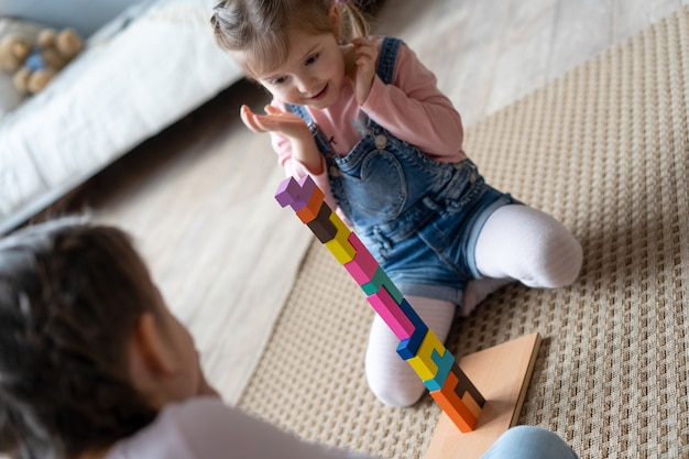 Enfants jouant avec des blocs de bois posés sur le sol dans leur chambre.