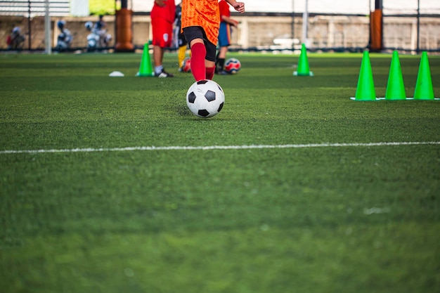 Enfants jouant le cône de tactique de ballon de football de contrôle sur le terrain d'herbe avec pour l'arrière-plan de formation Formation des enfants au football