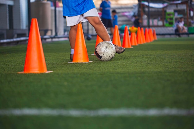 Enfants jouant le cône de tactique de ballon de football de contrôle sur le terrain d'herbe avec pour l'arrière-plan de formation Formation des enfants au football