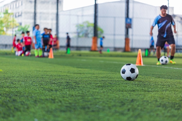 Enfants jouant le cône de tactique de ballon de football de contrôle sur le terrain d'herbe avec pour le fond de formation Formation des enfants au football