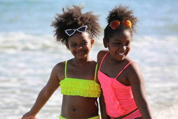 Enfants jouant courir sur le sable à la plage, un groupe d'enfants se tenant la main dans une rangée sur la plage en été, vue arrière contre la mer et le ciel bleu