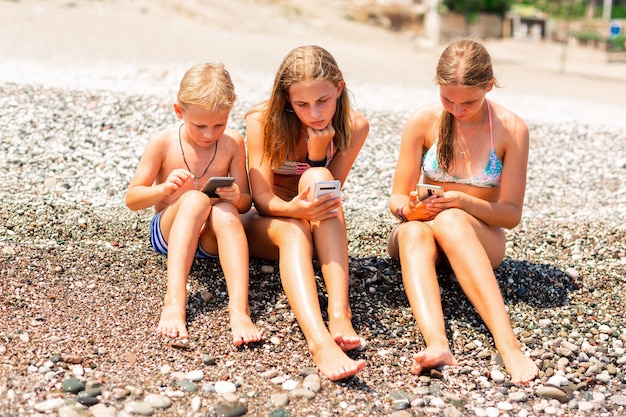 Enfants jouant à des jeux et recherchant le Web sur les téléphones à la plage