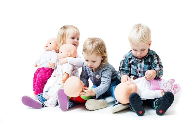 Enfants jouant avec des poupées. Le garçon et les filles sont assis par terre dans le jardin d'enfants et jouent à la famille. Notion de paternité