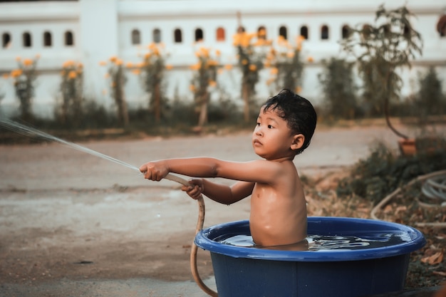 Les enfants jouent et baignent l&#39;eau dans le jardin, assis dans un seau d&#39;eau.