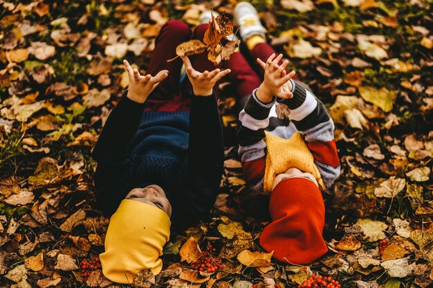 Photo des enfants joyeux et joyeux dans des vêtements chauds s'amusent à marcher, à courir dans le parc d'automne, à jouer avec des feuilles.