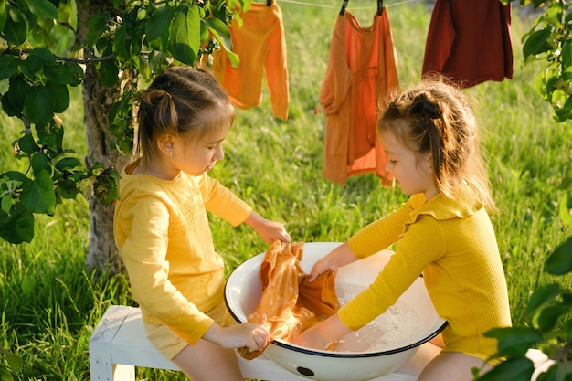 Les enfants lavent les vêtements dans un bassin sur un banc dans le jardin.