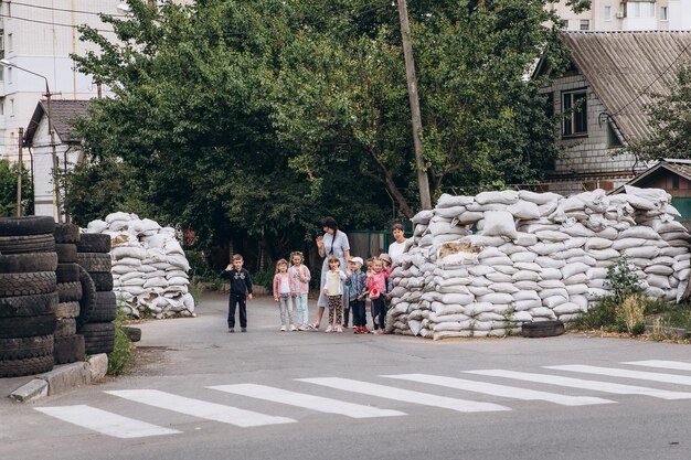 les enfants et leurs enseignants marchent par paires tenant un stylo et se cachent dans un barrage routier fait de sacs de sable