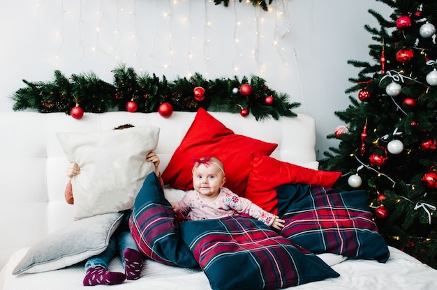 Enfants sur le lit dans la chambre près de l'arbre de Noël. Bonne année et joyeux Noël