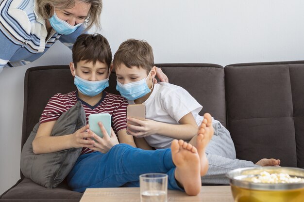 Enfants à la maison portant des masques médicaux et jouant sur les smartphones