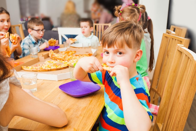 Enfants mangeant de la pizza à la table en bois, drôle de garçon regarde la caméra