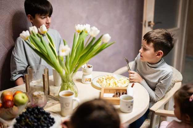 Les enfants mangent des fruits et des desserts boivent du thé à la maison dans la cuisine du soir Chocolat sur un bâton pour fondre