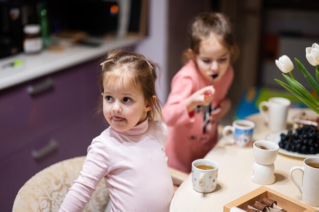 Les enfants mangent des fruits et des desserts boivent du thé à la maison dans la cuisine du soir