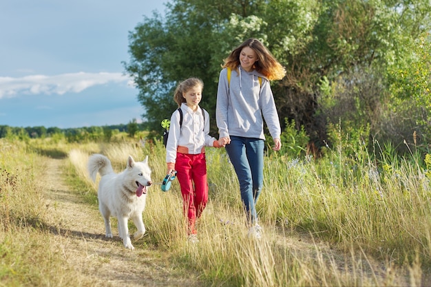 Enfants marchant avec un chien blanc dans le pré le jour de l'automne