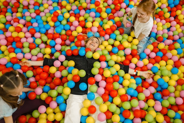 Enfants avec mère couchée parmi des boules colorées dans le centre de divertissement. Maman et sa fille loisirs en vacances, bonheur de l'enfance, enfants heureux sur l'aire de jeux