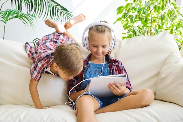 Enfants mignons avec des écouteurs appréciant la tablette à la maison