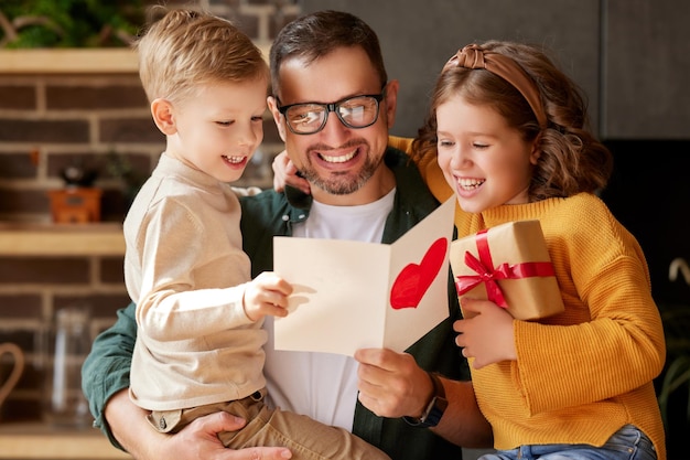 Enfants mignons félicitant papa heureux avec la fête des pères et lui donnant une carte postale de voeux faite à la main