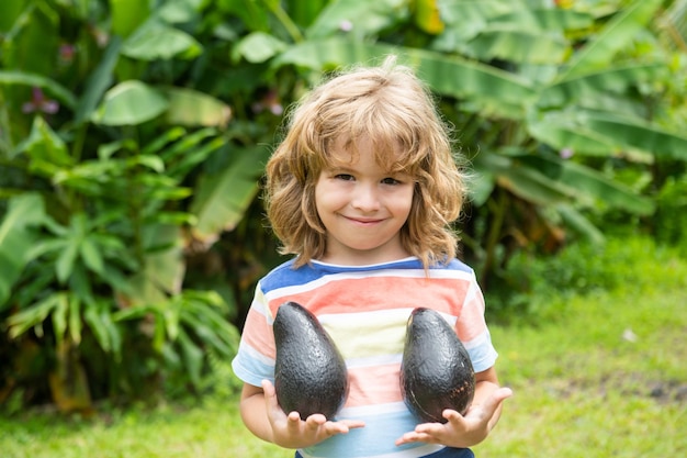 Enfants mignons ou garçon enfant souriant et tenant des fruits d'avocat.