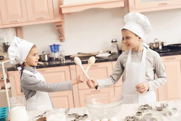 Enfants Mignons Jouent épées De Cuillères En Bois à La Cuisine.