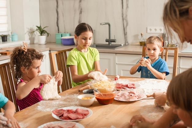 Les enfants mignons s'assoient à une table dans la cuisine et font de la pizza