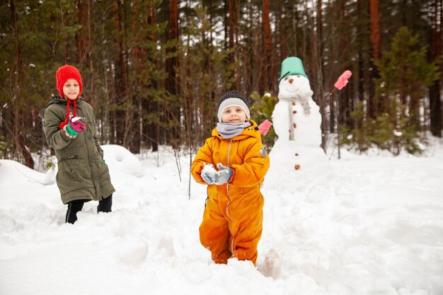 Enfants de neuf et trois ans en promenade hivernale près du bonhomme de neige