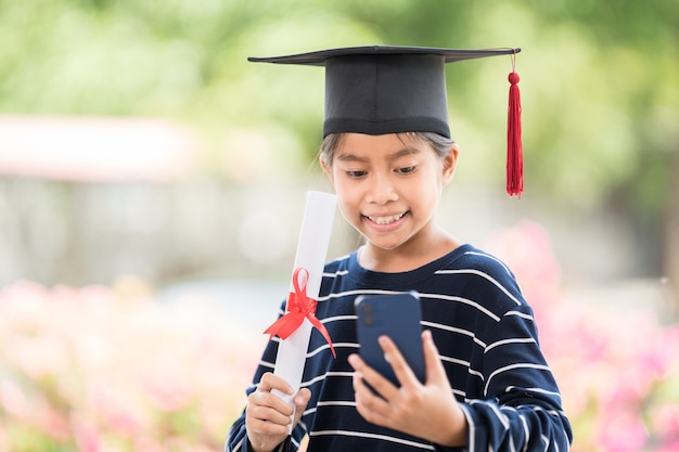 Photo les enfants obtiennent leur diplôme avec une casquette de remise des diplômes et un certificat de remise des diplômes roulé tenant un smartphone pour appeler