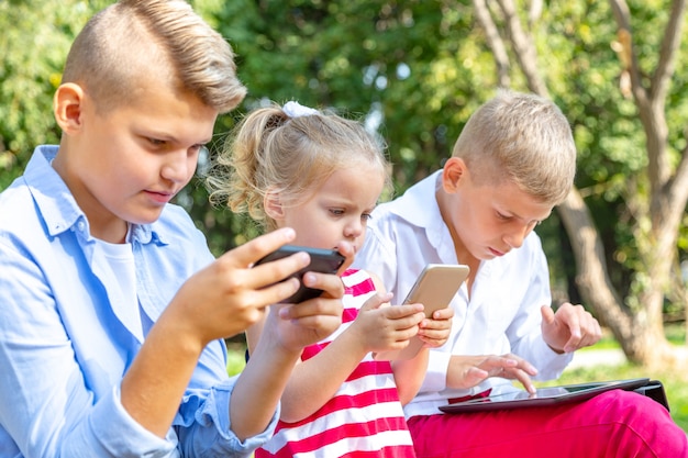 Enfants occupés à regarder leurs téléphones envoyer des SMS et jouer assis à l'extérieur