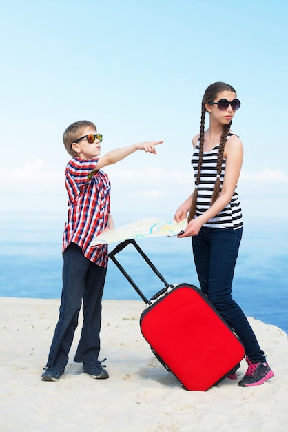 Enfants partant en vacances à la mer avec un bagage et une carte