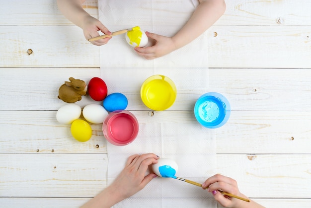 Les enfants peignent des œufs pour Pâques sur la table en bois