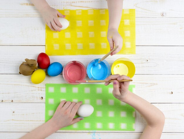 Les enfants peignent des œufs pour Pâques sur la table en bois