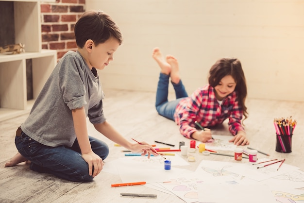 Les enfants peignent et sourient allongés sur le sol.