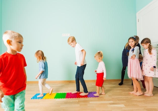 Les enfants pieds nus se tiennent dans une rangée entre des tapis en plastique tactiles de massage