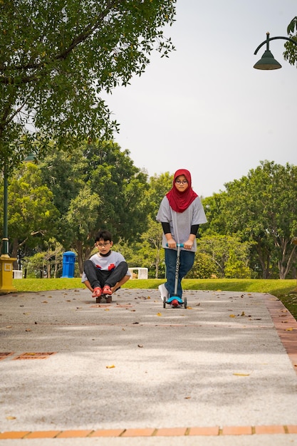 Photo des enfants à la planche à roulettes et au scooter dans le parc