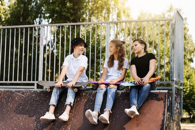 Les enfants avec des planches à roulettes et des penny communiquent et discutent sur le terrain de sport Concept d'amitié pour les enfants Les enfants sourient et rient et s'amusent ensemble