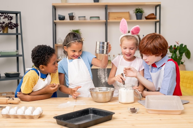 Enfants portant un tablier naviguant sur Internet sur une tablette numérique afin de trouver une recette de biscuit appétissant