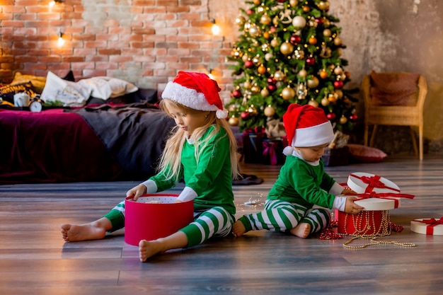 les enfants en pyjama et chapeaux de Noël déballent les cadeaux de Noël