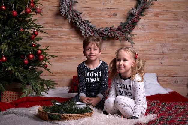 Enfants en pyjama jouant à la maison le soir des vacances de Noël. Heureux enfant sautant sur le lit.