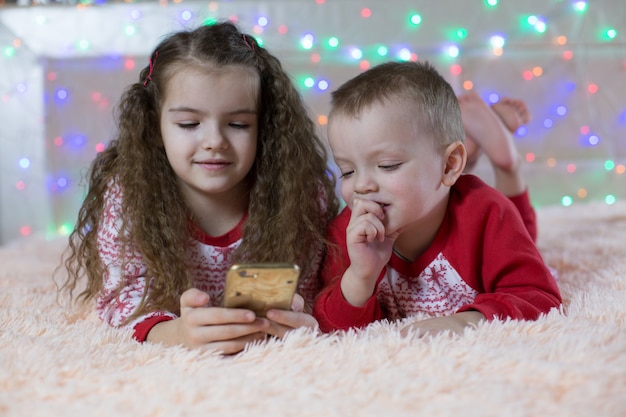 Enfants En Pyjama De Noël Jouant Smartphone