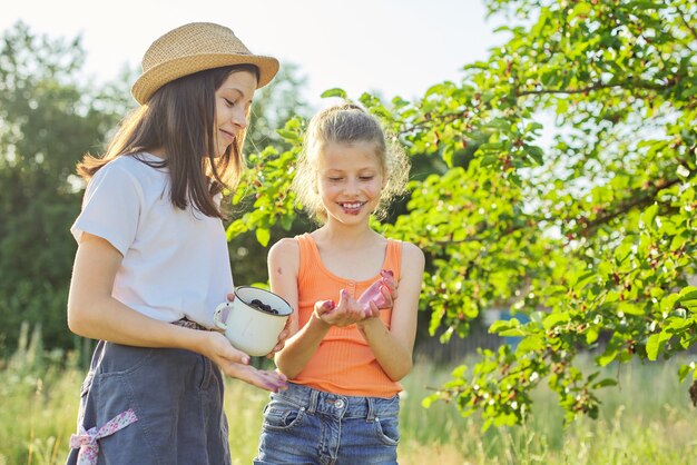 Enfants avec récolte de baies en mug, mûrier dans le jardin d'été. Baies naturelles sucrées savoureuses riches en vitamines