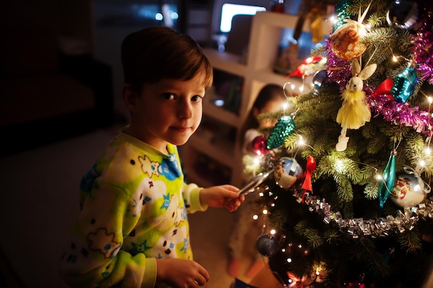 Enfants regardant sur l'arbre de Noël avec des guirlandes brillantes le soir à la maison.