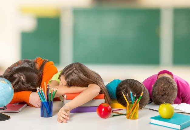 Enfants s'endormant sur la table tout en faisant leurs devoirs sur fond de classe