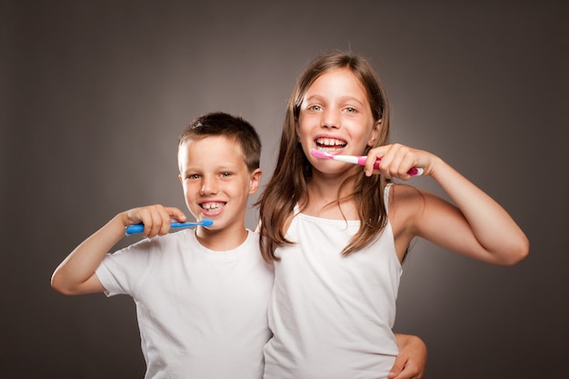 Enfants se brosser les dents sur un fond gris