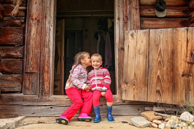 Enfants se reposant à la porte de la vieille maison en bois pendant les vacances d'été, concept de voyage respectueux de l'environnement