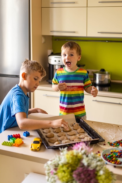 Enfants de sexe masculin drôles de frère se réjouissant de s'amuser à cuisiner un dessert avec des chocolats ronds multicolores mm